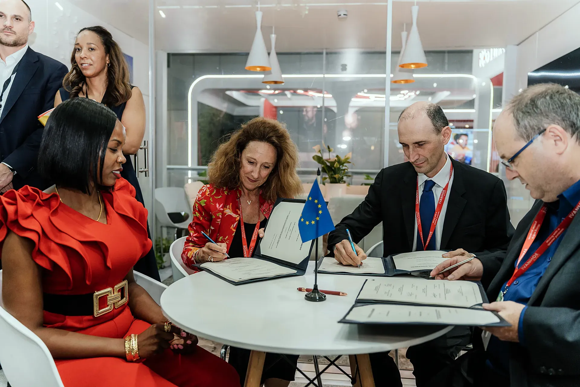 Delegates sign an agreement at a round table beside an EU flag