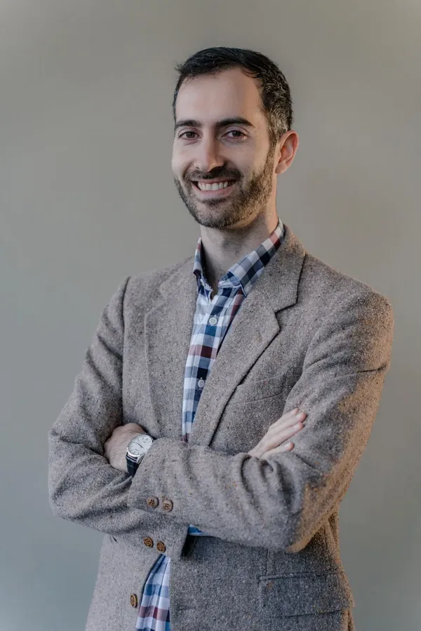 Corporate headshot of a smiling man in a tweed blazer, arms folded