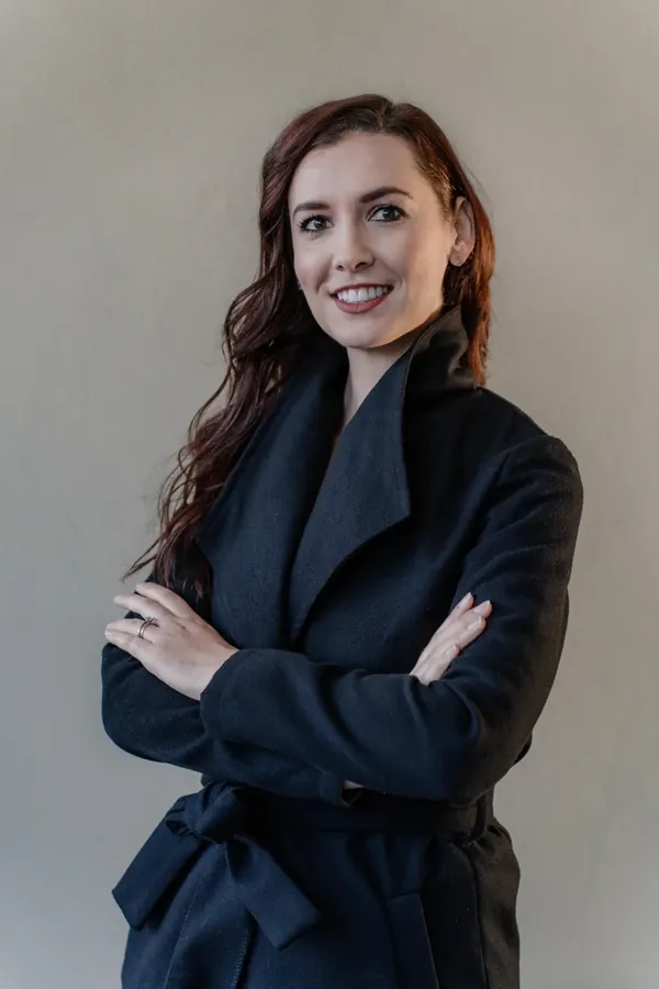 Corporate headshot of a smiling woman in a dark coat, arms folded