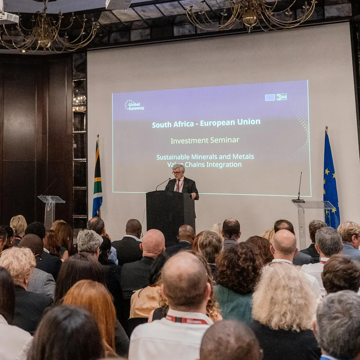 A keynote speaker at the podium in a hotel ballroom, addressing a full audience at a South Africa - European Union investment seminar