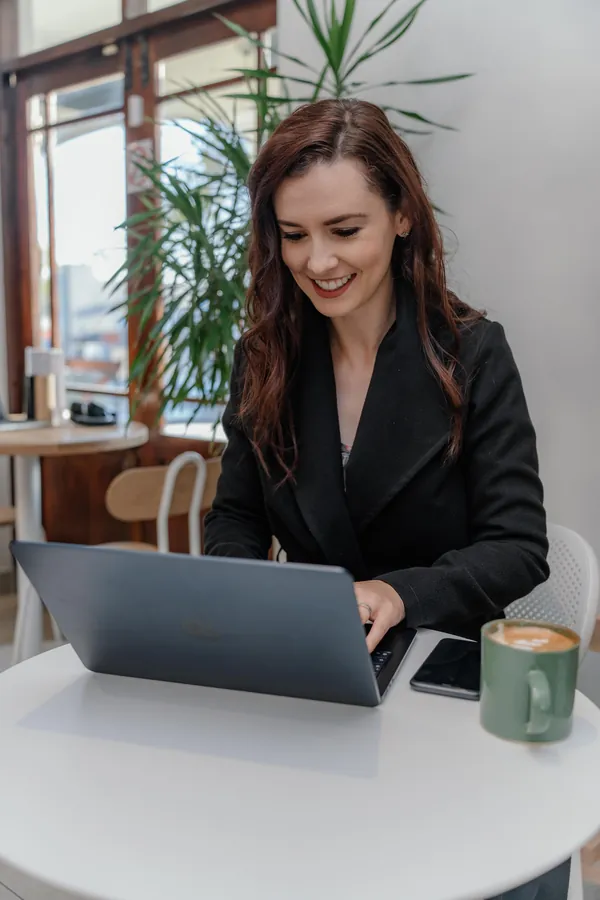 A businesswoman smiling as she works on her laptop at a cafe table