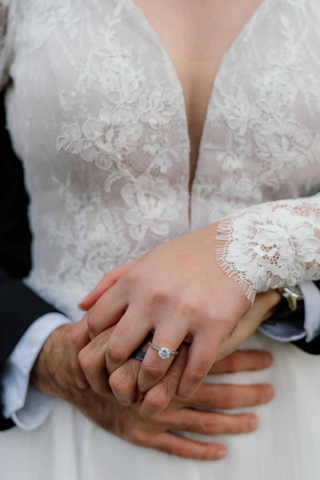 The bride's hand, with her engagement ring, resting over the groom's