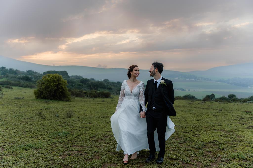 Bride and groom walking through an open field at sunset