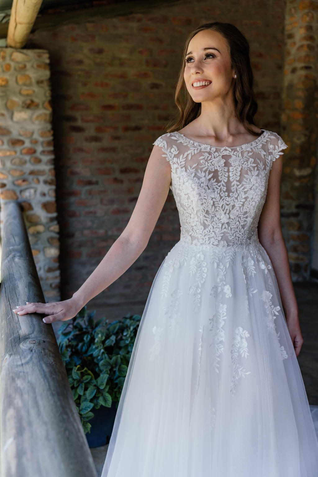 The bride in her lace gown smiling beside a stone pillar, Iain and Naomi's wedding