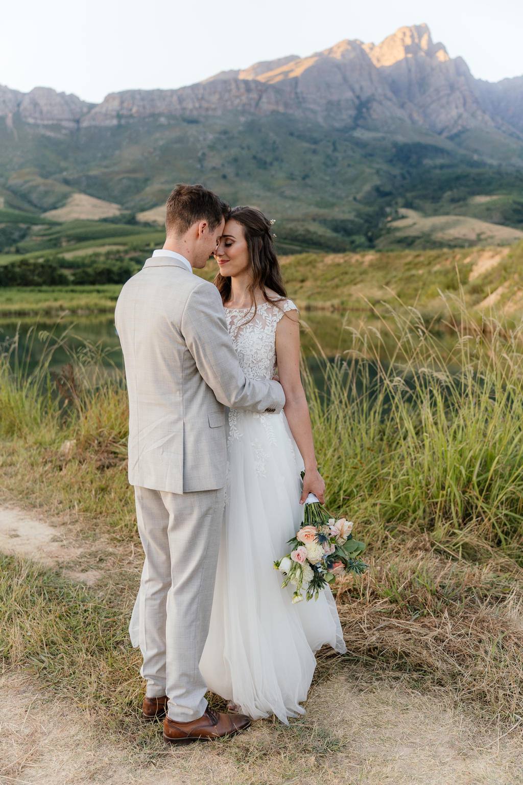 Bride and groom forehead to forehead on a farm track, the mountains behind them, Iain and Naomi's wedding