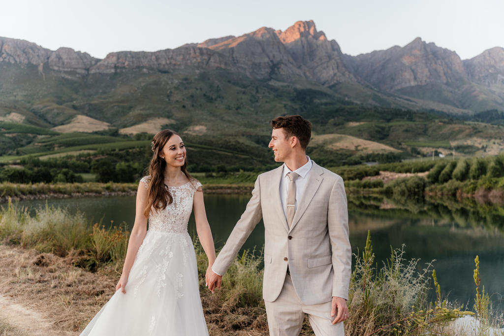 Bride and groom walking hand in hand beside a dam