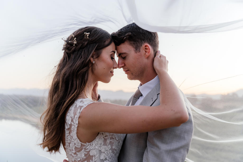 Bride and groom forehead to forehead under her veil at sunset