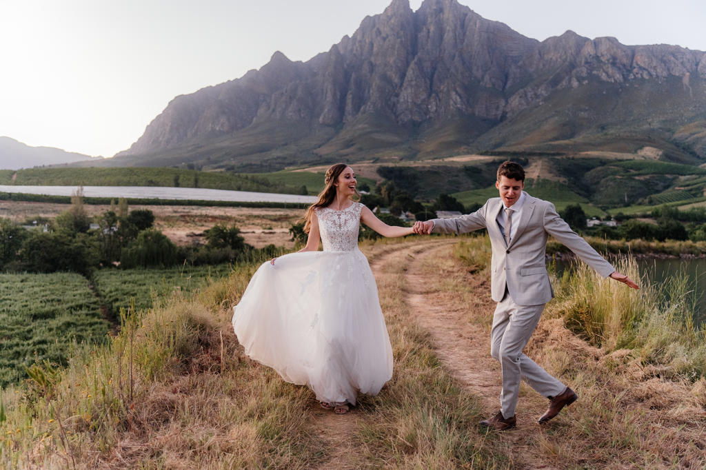 Bride and groom running hand in hand down a farm track