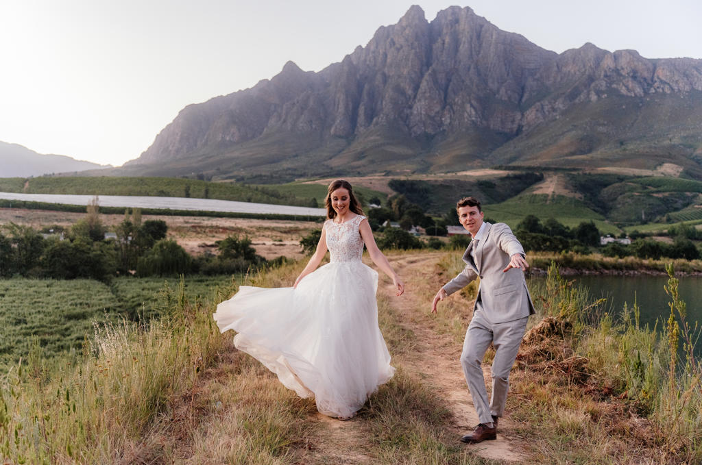 The bride twirling her dress as the groom dances towards her on a farm track, Iain and Naomi's wedding