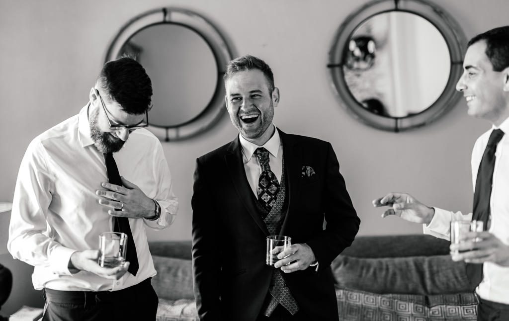 Black-and-white photo of the groom and groomsmen laughing over a whisky before the ceremony, Ian and Katharina's wedding