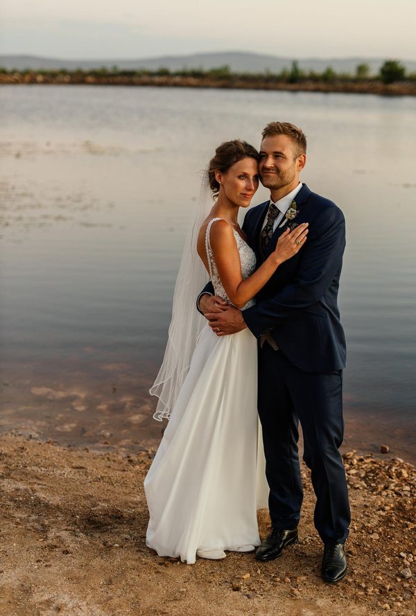 Bride and groom embracing at the edge of a dam at sunset