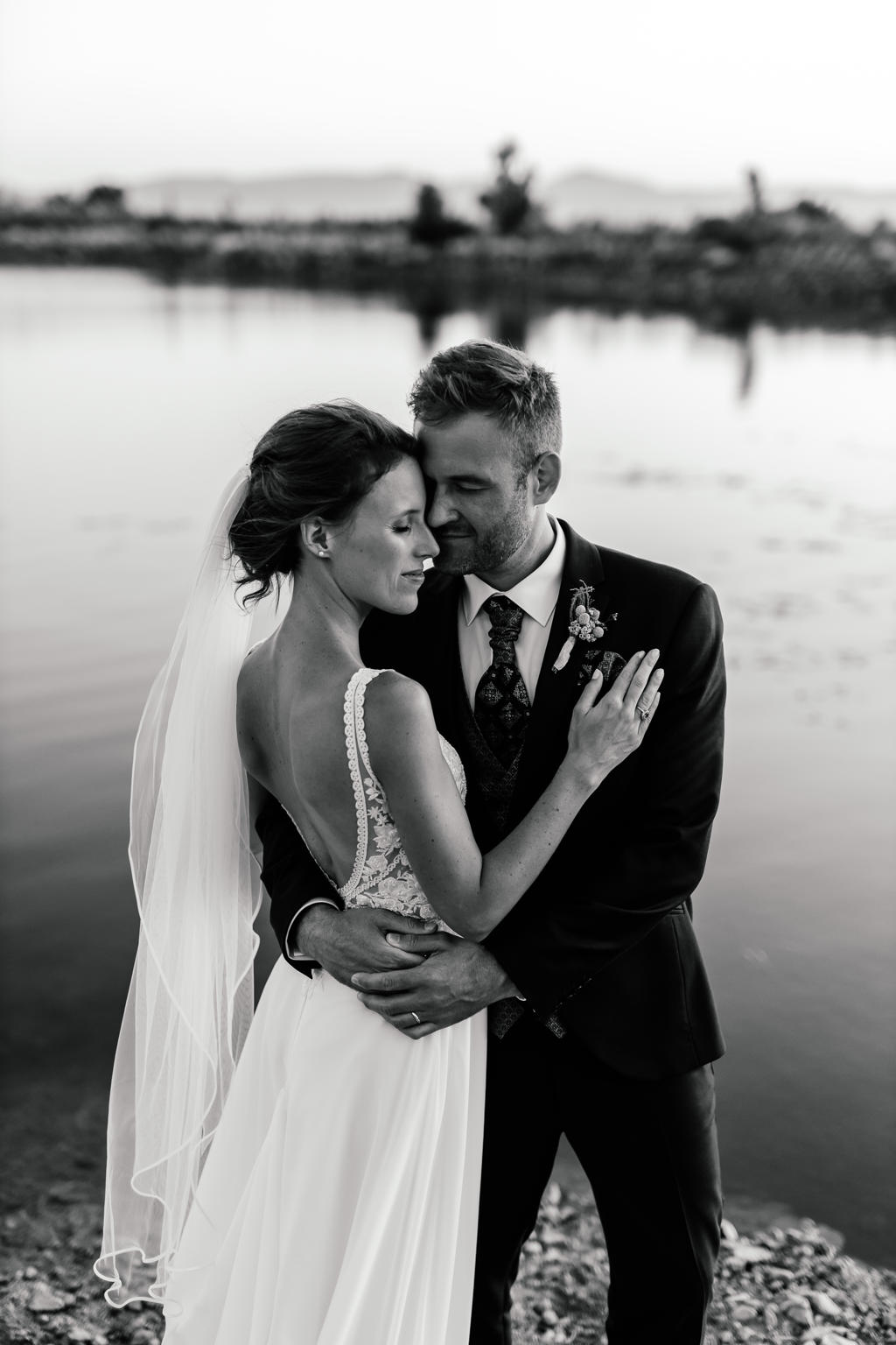 Black-and-white photo of the bride and groom cheek to cheek beside a dam, Ian and Katharina's wedding
