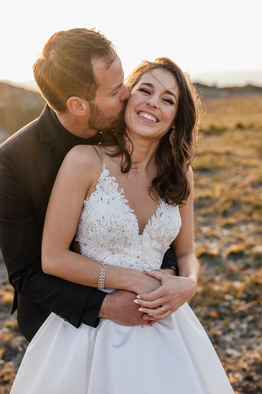 The groom kissing the bride's cheek from behind as she laughs in golden light, IW and Tarien's wedding