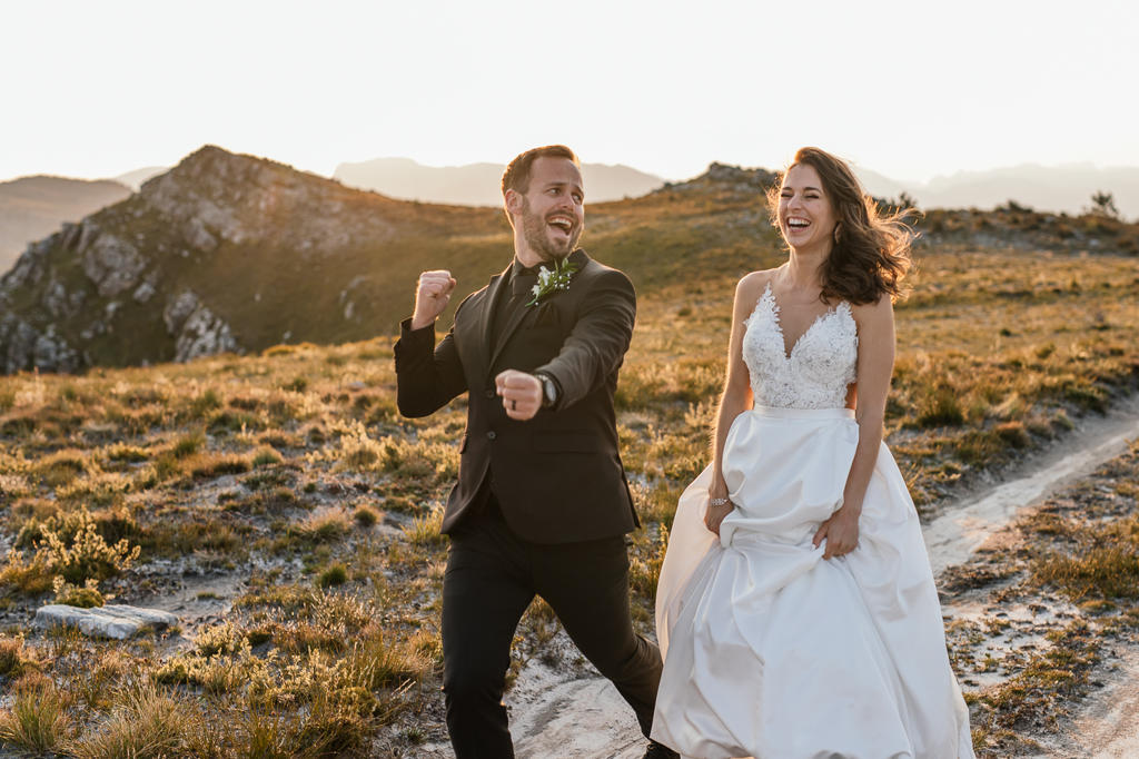 Bride and groom laughing on a ridge in golden evening light