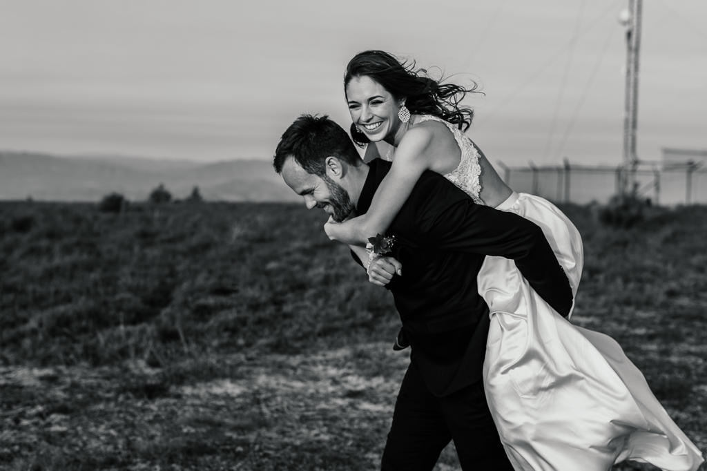 Black-and-white photo of the groom giving the bride a piggyback, both laughing, IW and Tarien's wedding