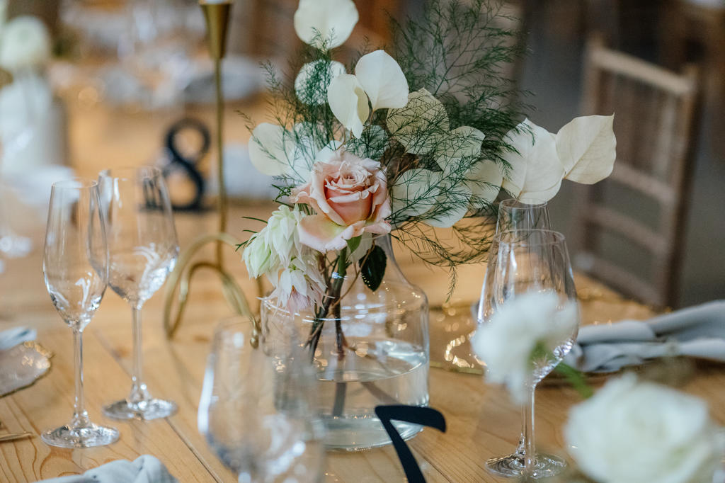 A blush rose and white blooms in a glass vase on a set reception table, Ulrich and Keshia's wedding