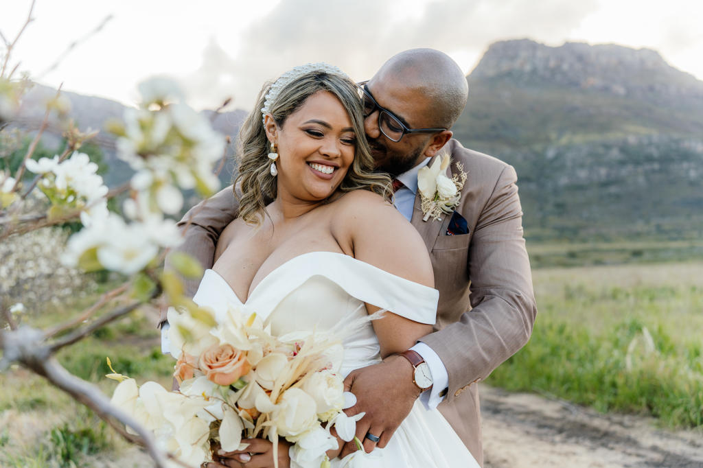 Groom kissing his bride among blossom trees below the mountains