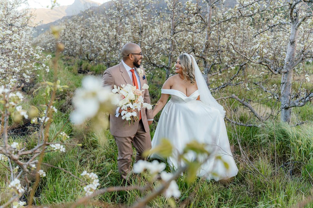 Bride and groom walking hand in hand through a blossoming orchard