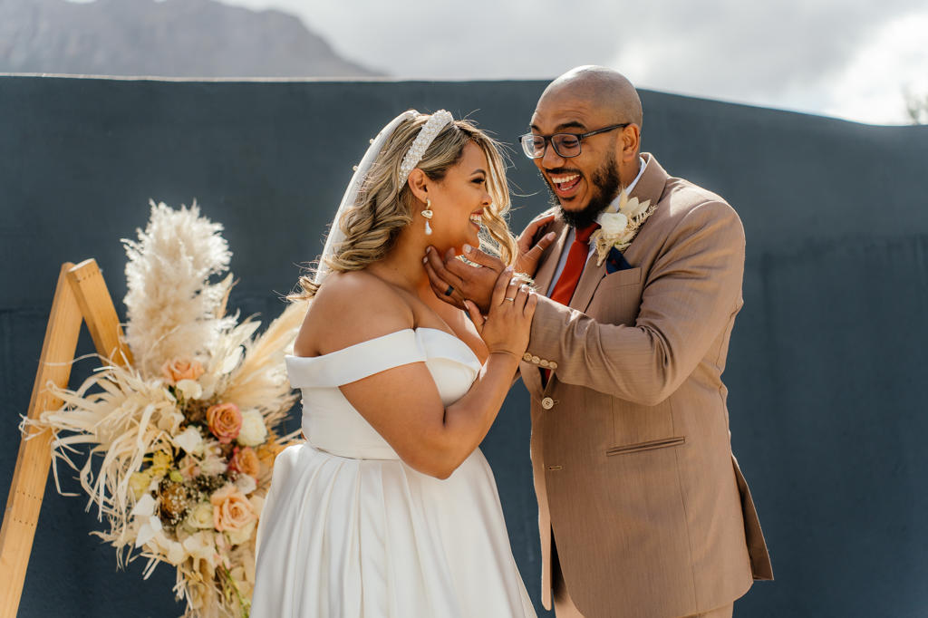 Bride and groom laughing together beside a dried-flower display