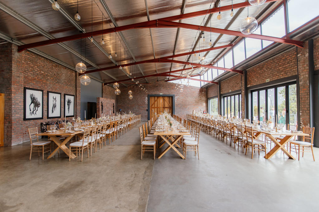 The reception hall set with long wooden tables under a red steel roof, Ulrich and Keshia's wedding