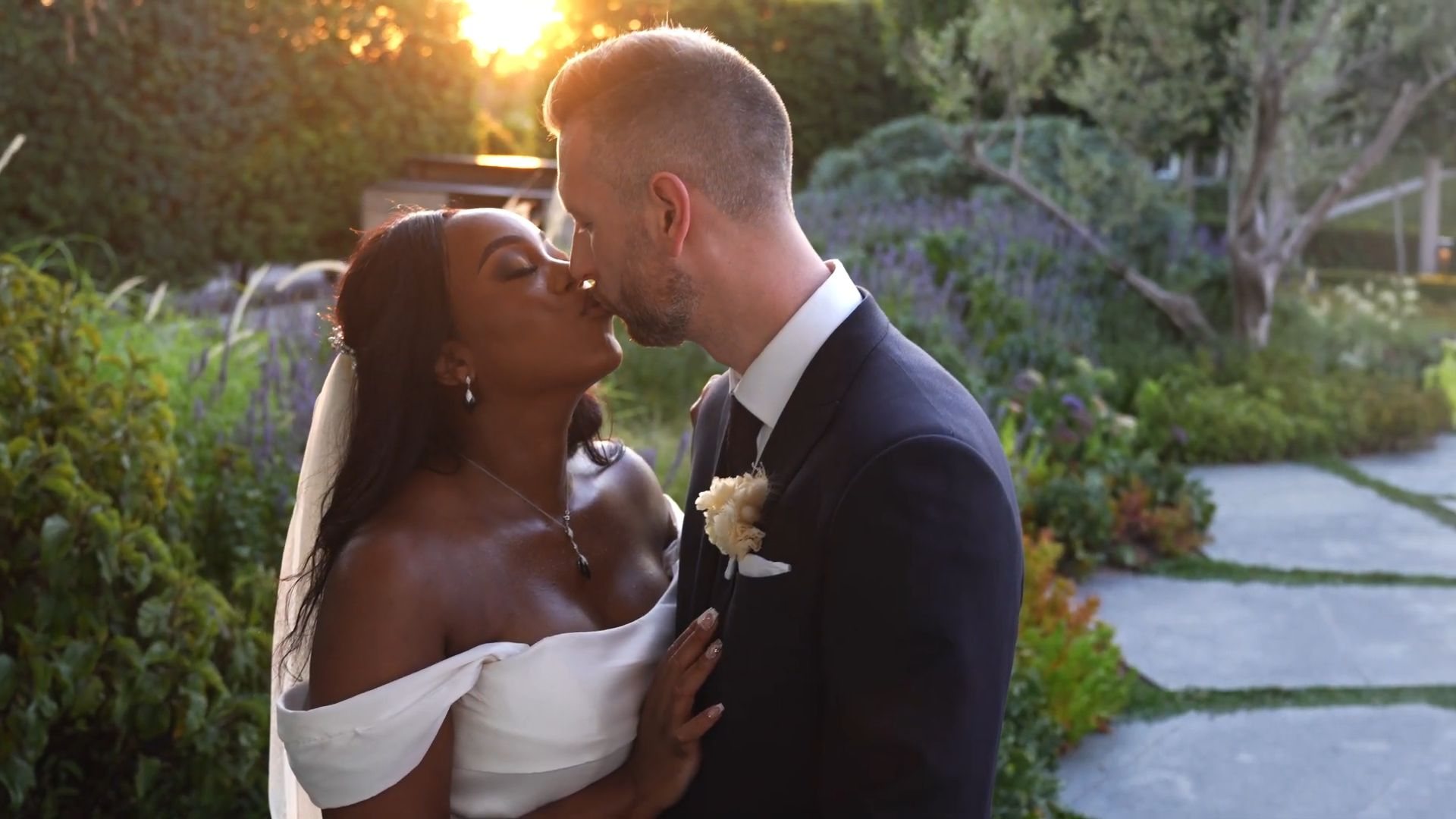 Anthony and Annie kissing in the garden with the setting sun behind them