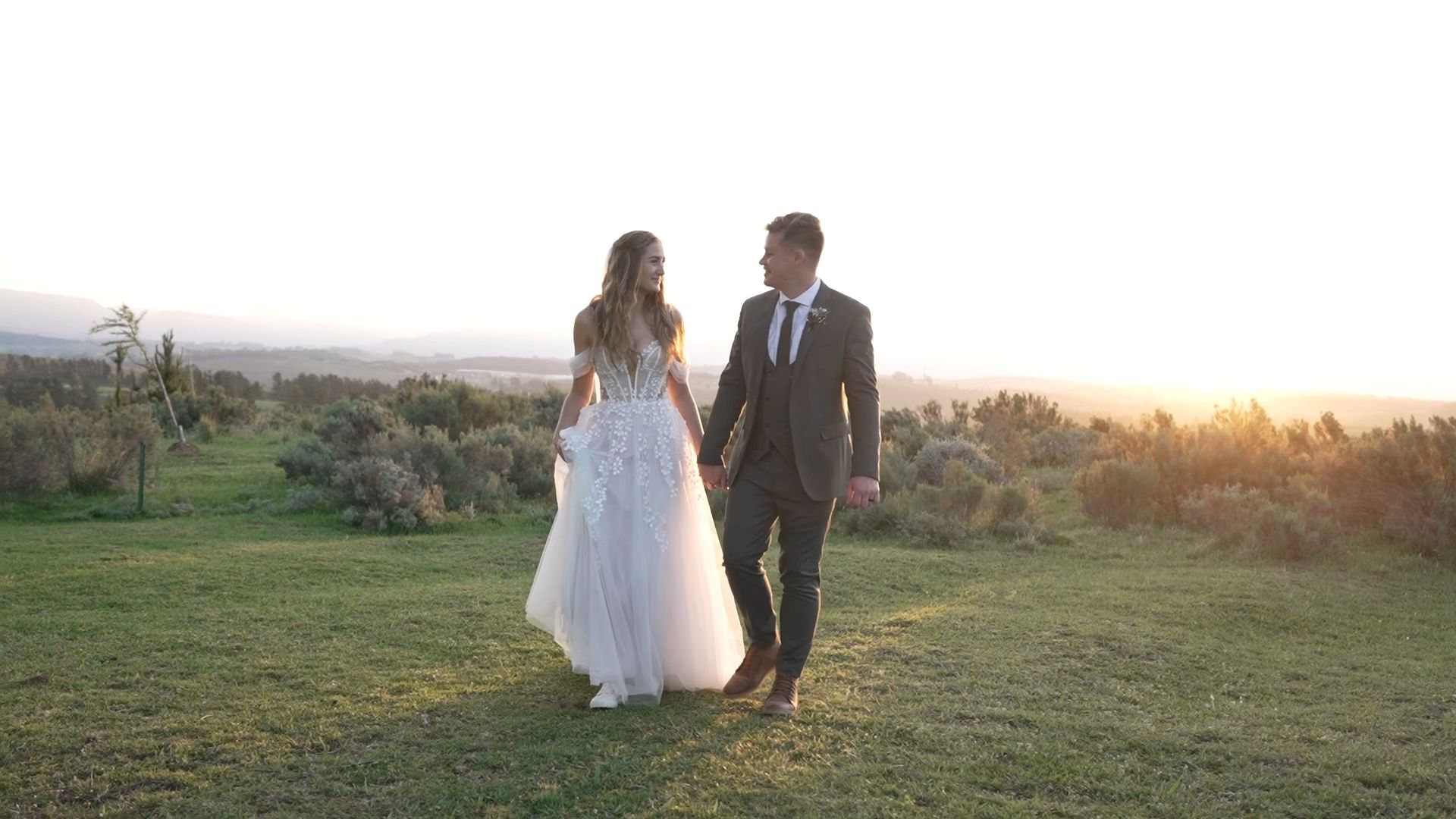 Douw and Claudia walking hand in hand across the field at sunset