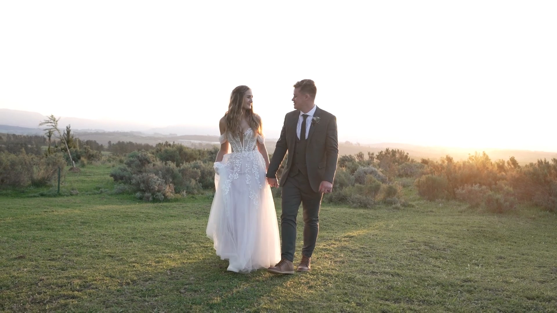 Douw and Claudia walking hand in hand across a field at sunset, a still from their wedding film