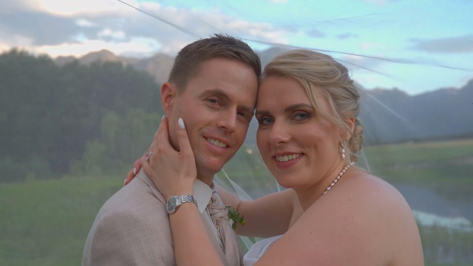 Henry and Kathrin cheek to cheek under her veil, smiling, with the mountains behind them
