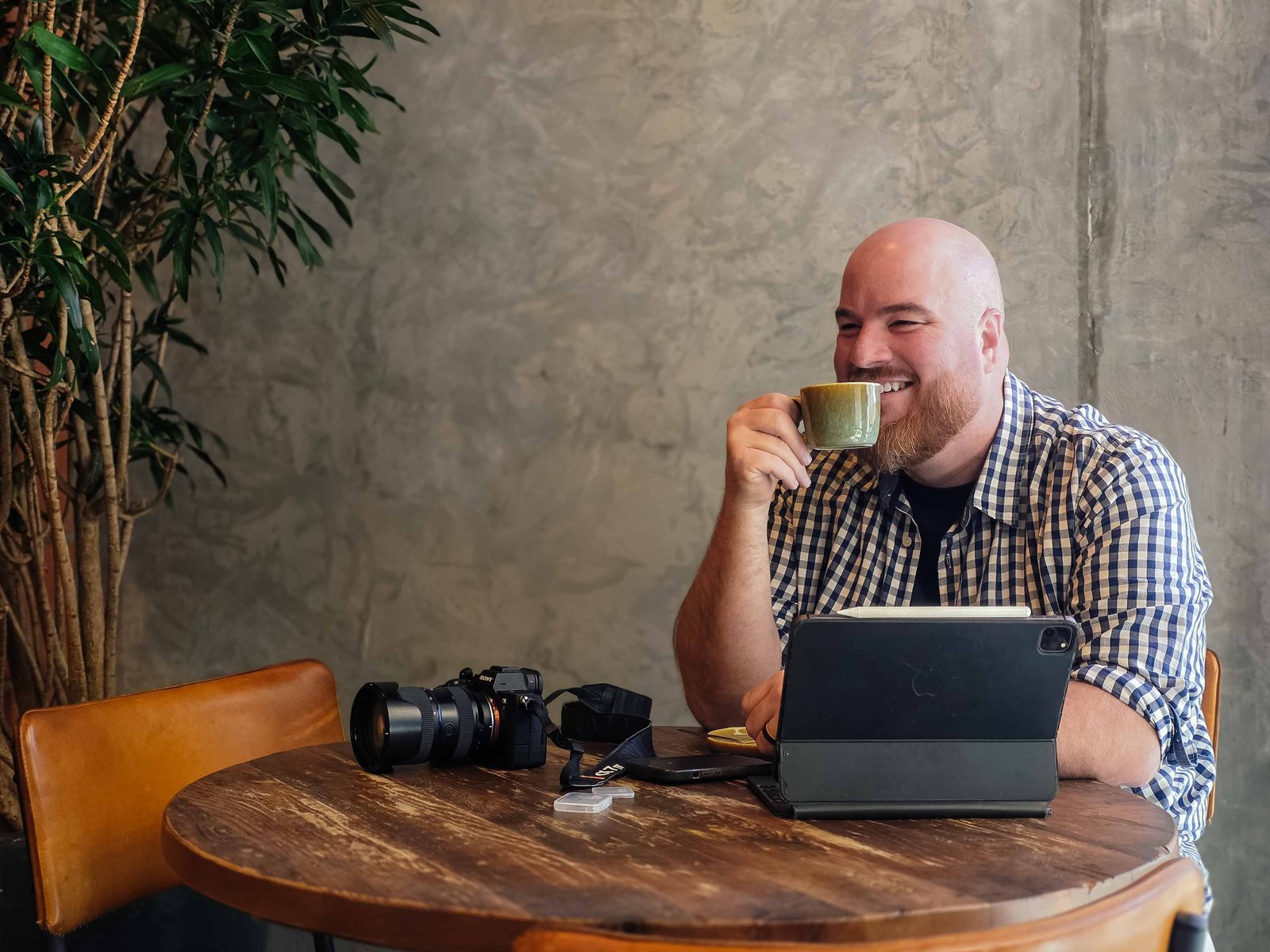 Kobus smiling over a cup of coffee at a café table, his camera and tablet in front of him