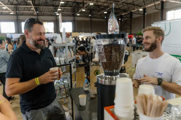 The barista smiling behind the grinder as a customer looks on, Kort Coffee