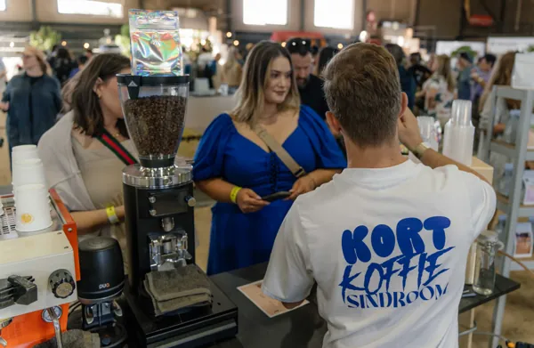 The barista in a Kort Koffie shirt talking customers through the grinder