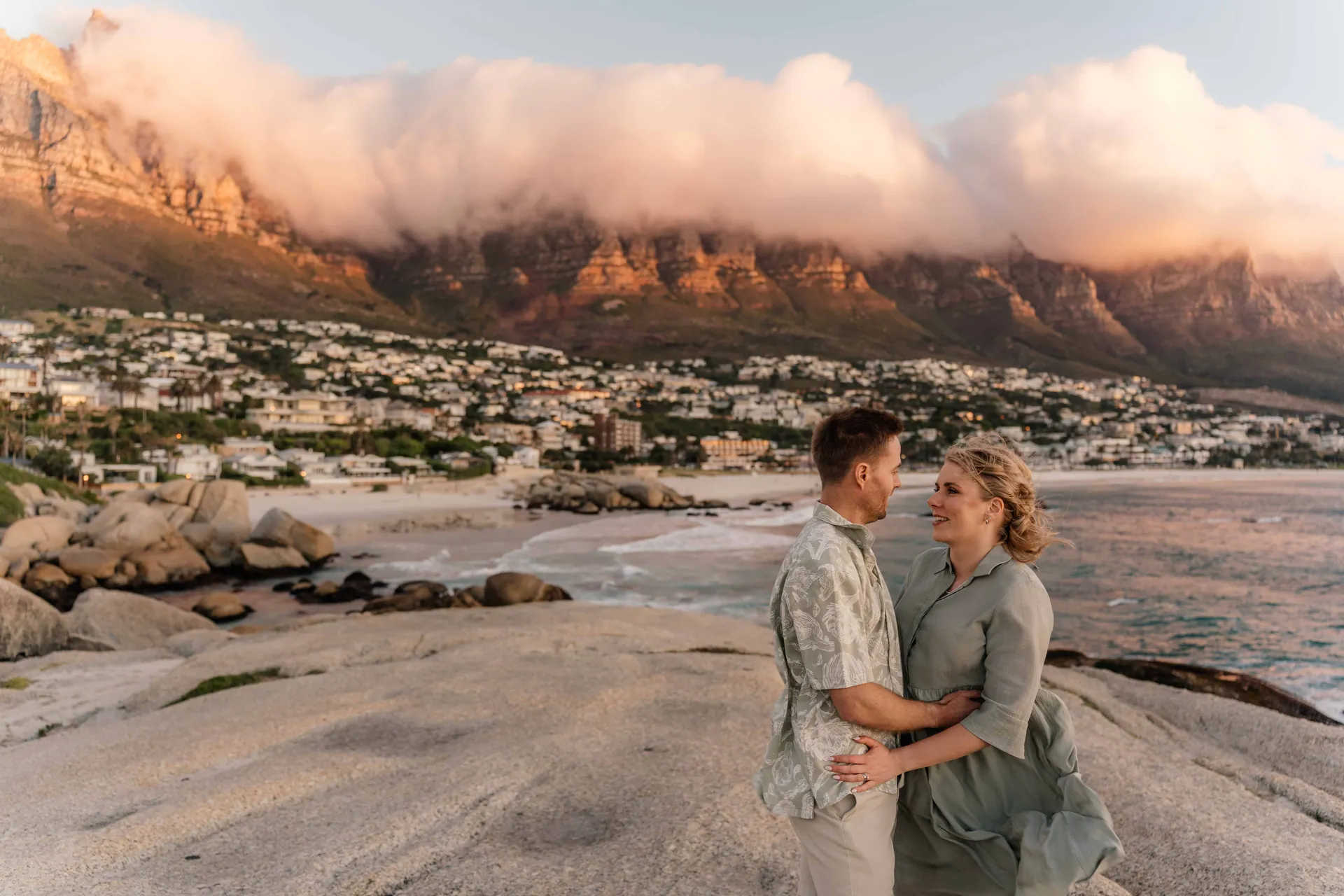 An engaged couple embracing on granite boulders at sunset with the Twelve Apostles behind them, Henry and Kathrin