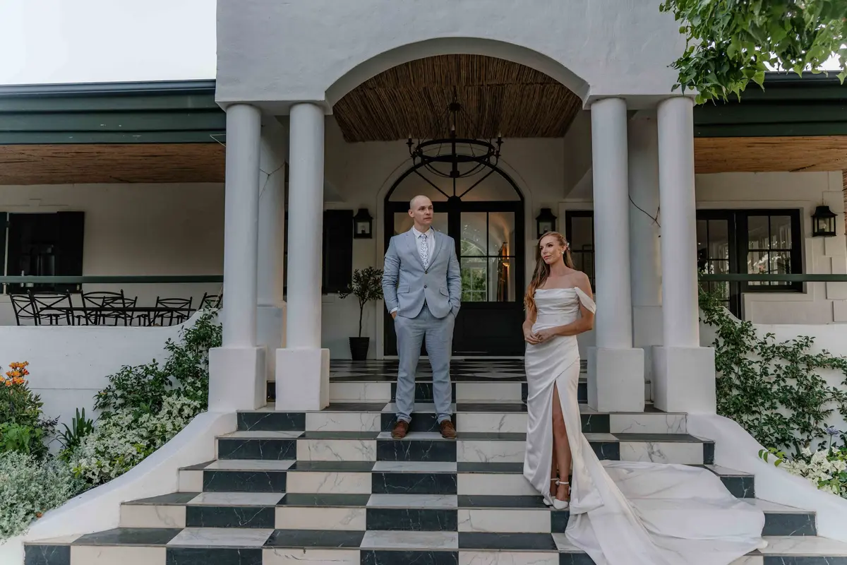A bride and groom on the chequered steps of the venue under the oaks